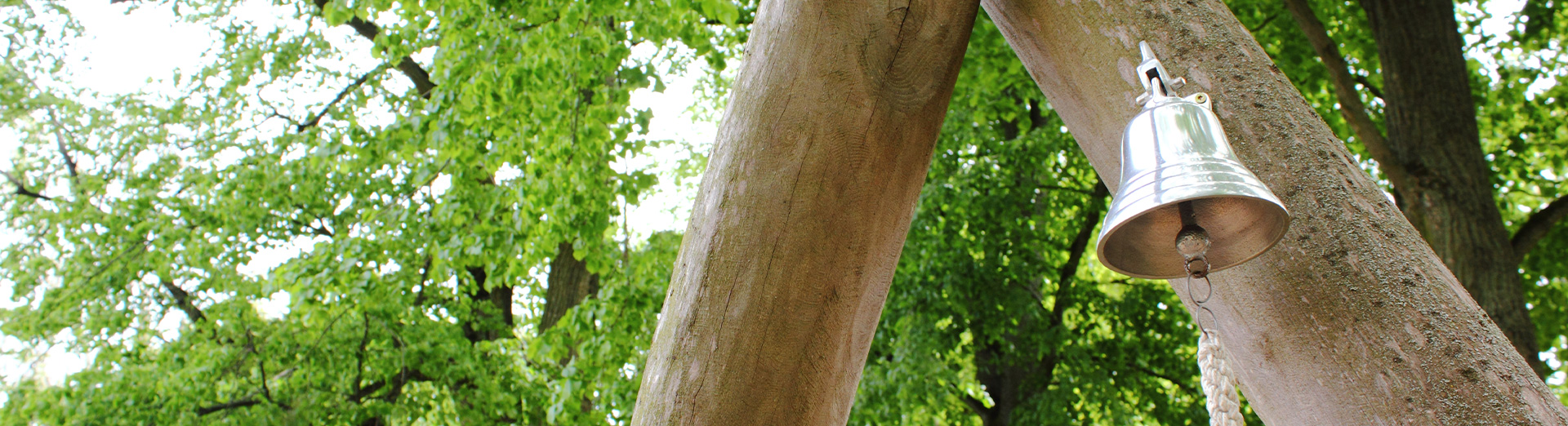 Metallglocke draußen an einem Holzstamm