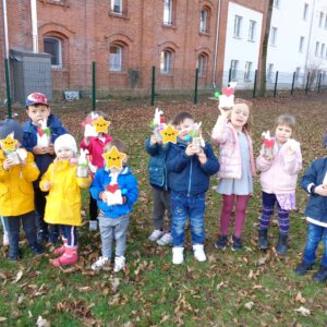 Kindergartengruppe steht auf einer Wiese und halten ihr Osternest in die Kamera. Alle lachen dabei