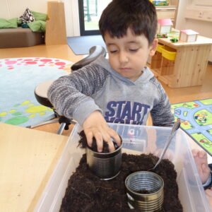 Kleiner Junge mit dunklen Haaren, bepflanzt sein Osternest mit Grassamen