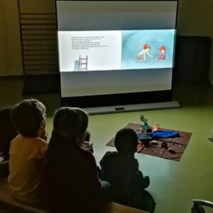 Kinder sehen sich ein Bilderbuchkino auf einer Leinwand an.