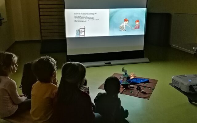 Kinder sehen sich ein Bilderbuchkino auf einer Leinwand an.