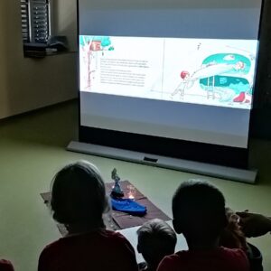 Kinder sehen sich ein Bilderbuchkino auf einer Leinwand an.