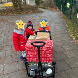 Kinder schieben einen Bollerwagen voller Weihnachtspäckchen.