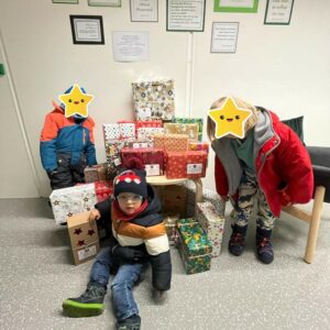 Kinder sitzen und stehen neben verpackten Weihnachtsgeschenken.