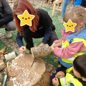 Drei Kinder schauen sich mit einem Erwachsenen ein Stück Holz genauer an